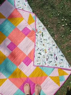 someone is laying down on the grass with their feet propped up next to a quilt