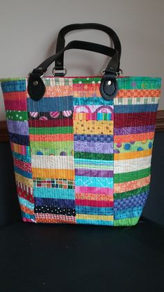 a multicolored handbag sitting on top of a black table next to a wall