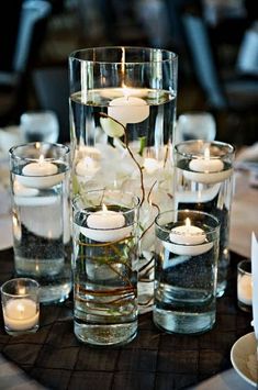 there are many candles in the glass vases on the table with flowers and water