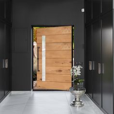 a vase with flowers sitting on the floor in front of a wooden door and black cabinets