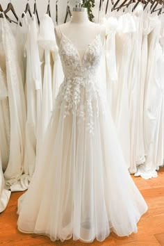 a white wedding dress is on display in front of other brides dresses and gowns