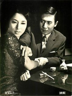 an old black and white photo of two people holding each other's arm while sitting at a table