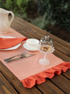 a table topped with plates and silverware on top of a wooden table next to a pitcher