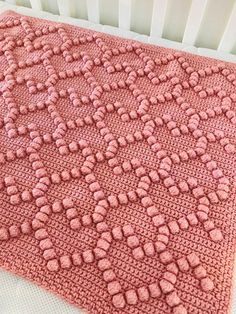 a pink crocheted blanket sitting on top of a bed