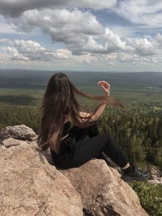 a woman with long hair sitting on top of a rock