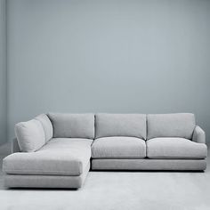 a large gray couch sitting in front of a white wall with a lamp on it