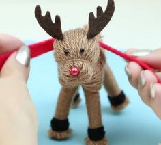 someone crocheting a reindeer ornament with red yarn on it's antlers