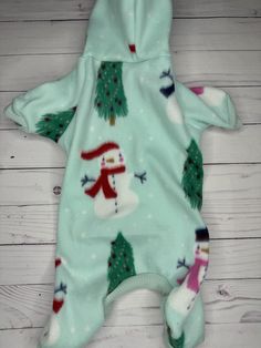 a baby's snowman outfit laying on top of a white wooden floor next to a christmas tree