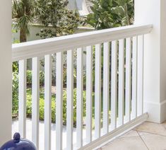 a blue vase sitting on top of a white porch next to a fence and palm trees