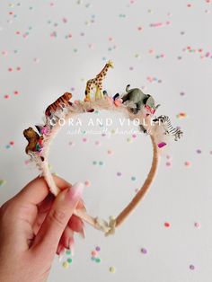 a hand holding a small headband with animals on it and confetti scattered around