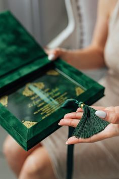 a woman is holding a green box with a tassel