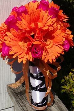 an orange and pink flower in a black and white vase on a wooden bench outside