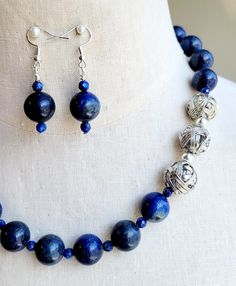 Make a statement in this one-of-a-kind lapis lazuli and silver beaded necklace and earrings set. Polished 14mm round Lapis Lazuli stone balls are strung with matching, faceted, lapis stone crystals and accented with shiny silver-plated beads all strung on wire.   The necklace is finished with stainless-steel chain and a silver-plated lobster clasp. The necklace measures 20 inches long. Matching stone beaded earrings are strung on 925 silver ear wires. Blue Lapis Lazuli Jewelry With Large Beads, Artisan Lapis Lazuli Jewelry With Polished Beads, Lapis Lazuli Beaded Necklaces With Large Beads As Gift, Lapis Lazuli Beaded Necklace With Large Beads For Gift, Handmade Sodalite Round Bead Necklaces, Artisan Lapis Lazuli Gemstone Beads Jewelry, Handmade Sodalite Round Beads Necklace, Lapis Lazuli Gemstone Beads Jewelry, Blue Polished Beads Jewelry