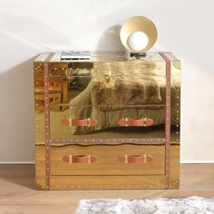 a mirrored chest with two drawers and a gold bed in the middle on a wooden floor next to a white rug