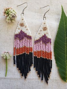 two pairs of beaded earrings sitting on top of a table next to a flower