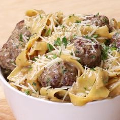 a white bowl filled with pasta and meatballs covered in parmesan cheese on top of a wooden table