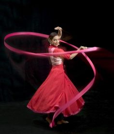 a woman in a red dress is holding a pink ribbon and spinning it with her hands