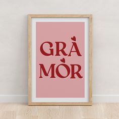 a framed poster with the words gra mor in red on a white wall next to a wooden floor