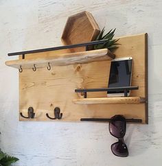 a wall mounted shelf with hooks and sunglasses on it, next to a potted plant