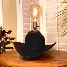 This lamp memorializes that bright idea moment when a lightbulb appears above your head. A high-quality classic felt cowboy hat, this piece will add warm light to a room of any decor. Made with an antique brass dimmable socket with vintage style LED light, 7' rayon wrapped cord, wood base with non-scratch felt furniture pad, and heavy-duty copper and steel parts to hold it all together.  Includes: Lamp Hat, Vintage LED dimmable bulb, Collapsable Felt Carrying Case, and Hat Cleaning Sponge Cowboy Lamp, Black Felt Cowboy Hat, Hat Cleaning, Felt Furniture, Felt Cowboy Hat, Cord Wood, Felt Cowboy Hats, Cleaning Sponge, Furniture Pads