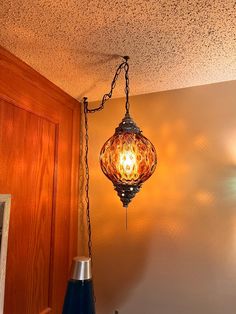 a lamp hanging from the ceiling next to a vase on a table with an object in front of it