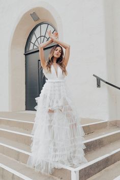 a woman in a white dress standing on some steps with her arms up and hands behind her head