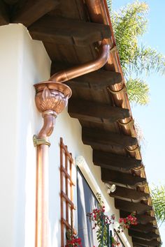 the corner of a building with a copper colored pipe on it's side and potted plants in front