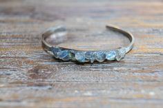 "Gemstone open gold or silver bangle with pieces of light gray Labradorite with flashes of blue and green. The setting is on a long rectangle that is 2\" long and a little under 1/4\" narrow, it is petite and slim. The cuff is gold or silver plated stainless steel and adjustable, 2\" x 2 1/2\" circumference.  The bracelet is made with natural stone each one has slight variations in size and shape. Your bracelet will be unique." Silver Moonstone Bangle, Silver Fusion Bracelets Hand Wrapped, Unique Labradorite Bangle Jewelry, Handmade Labradorite Bangle Jewelry, Silver Hand Wrapped Fusion Bracelets, Labradorite Bracelet Jewelry Gift, Fusion Style Silver Hand Wrapped Bracelets, Blue Labradorite Bracelet, Silver Labradorite Gemstone Bracelets