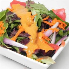 a salad in a white bowl topped with cheese and lettuce, carrots and onions