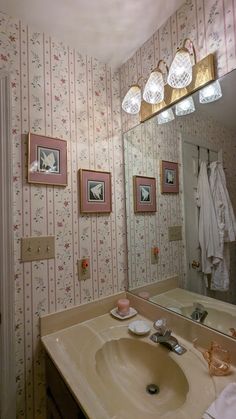 a bathroom sink sitting under a mirror in front of a wall papered wall with pictures on it