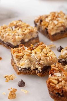 several pieces of dessert sitting on top of a white tablecloth covered in chocolate chips and nuts