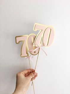 a person holding up a pink 70th birthday cake topper with the number seventy on it