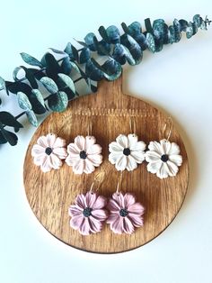 three flower earrings sitting on top of a wooden board next to a string of beads