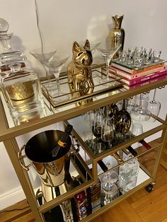 a gold bar cart filled with glasses and liquor bottles on top of a hard wood floor