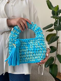 a woman holding a blue woven purse with tassels