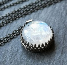 The gorgeous moonstone in this necklace glows with its own internal light, reflecting blue flashes. The simple round shape of the stone is reminiscent of a shining full moon. The 16mm stone is held in a patterned sterling silver bezel setting, open on the back to let in extra light and to show off the gorgeous colors reflected on the back of the stone. The pendant is hung on a sterling silver chain, available in your choice of 16, 18, or 20 inches. The necklace has been oxidized and brushed, giv Ethereal Round Birthstone Jewelry, Moonstone Gemstone Crystal Necklace With Round Pendant, Spiritual Round Crystal Necklaces With Moon Phase, Ethereal Moon Phase Jewelry For Gift, Ethereal Moon-shaped Jewelry Gift, Mystical Moonstone Round Pendant Jewelry, Silver Round Crystal Necklaces Mystical Style, Moonstone Round Necklace For Gifts, Handmade Celestial Crystal Necklace