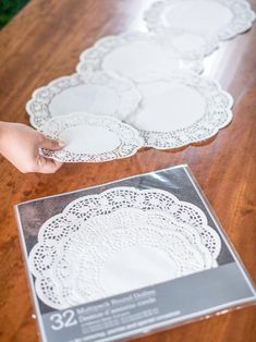 the table is covered with white doily on it's sides and there are two hands reaching for one