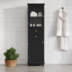 a tall black cabinet next to a potted plant in a white room with tiled walls