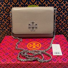 Nwt Auth Tory Burch Britten Chain Wallet Color Is French Gray Logo Is Hammered Silver Metal The Strap Has Leather Intertwined In The Metal Pebbled Leather Front Flap With Double Magnetic Snap Closure 1 Exterior Slip Pocket On Back 2 Interior Slip Pockets, 8 Card Slots, 1 Zip Pocket. Logo Lining Strap With (Approx.) 23" Drop Approximate Measurements 5.5" H X 7.5"L X 1.5" Silver Leather Wallet On Chain With Chain Strap, Silver Rectangular Wallet On Chain With Strap, Elegant Silver Leather Wallet On Chain, Rectangular Wallet On Chain With Silver-tone Hardware, Everyday Wallet On Chain With Palladium Hardware, Silver Rectangular Wallet On Chain For Everyday Use, Silver Wallet On Chain For Everyday Use, Silver Rectangular Wallet With Silver-tone Hardware, Rectangular Silver Wallet With Silver-tone Hardware