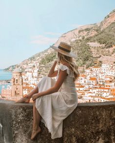 a woman sitting on top of a stone wall next to a body of water with buildings in the background