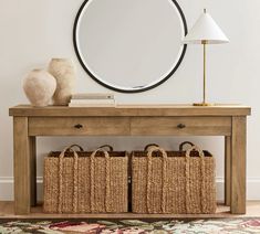 a console table with two baskets under it and a round mirror on the wall behind it