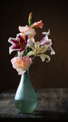 a blue vase filled with pink and white flowers on top of a wooden table next to a brown wall