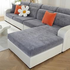 a large gray couch with orange pillows and a white flower on the end table in front of it