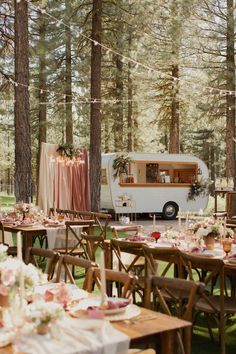 a food truck parked in the middle of a forest with tables and chairs set up