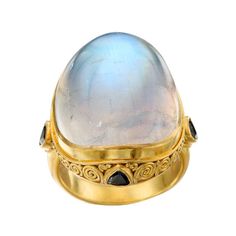 A signature classic Steven Battelle cocktail ring with a huge 19 x 24 mm shimmering oval rainbow blue moonstone cabochon and a carat of trillium faceted blue sapphires set in a handmade ancient-inspired "spirals and jawan" 18K gold setting. Rainbow moonstone is believed to help strengthen intuition and psychic perception, especially offering us visions of things that aren't immediately obvious. This ring is a SHOWSTOPPER that will be commented on by everyone who sees it. Currently sized 7, this Strengthen Intuition, 22k Gold Ring, Sapphire Cocktail Ring, Modern Bracelets, Gold For Sale, Gold Cocktail Ring, Blue Moonstone, Rainbow Moonstone Ring, Large Ring