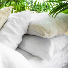 white pillows stacked on top of each other in front of green plants and trees behind them