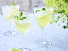 three glasses filled with drinks sitting on top of a white table covered in green flowers