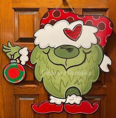 a door hanger with a green monster wearing a santa hat and holding a christmas ornament