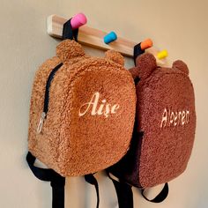 two teddy bears are hanging on the wall with their name written on them and one has a back pack attached to it