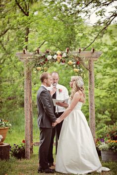 a bride and groom are standing under an arbor with flowers on the branches in front of them